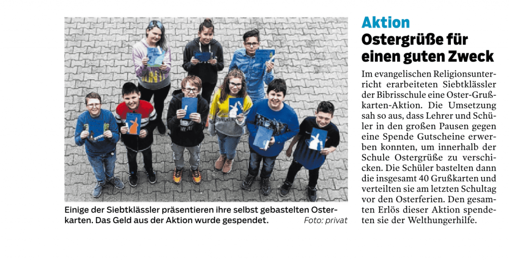 Eine Gruppe lächelnder Schüler steht draußen auf einer gepflasterten Fläche. Jeder hält selbstgemachte blaue und gelbe Karten in den Händen. Sie sind im Halbkreis angeordnet und blicken in die Kamera. Die Karten zeigen Ostermotive.