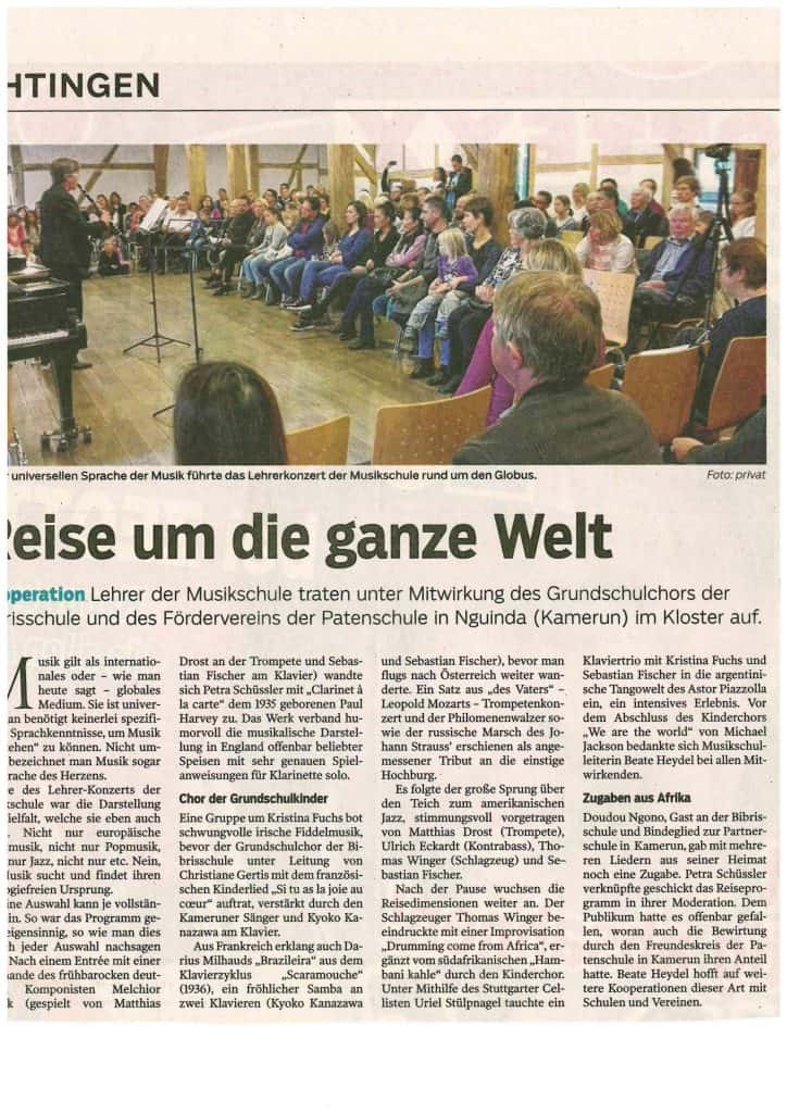 Eine Gruppe von Menschen sitzt in Stuhlreihen und verfolgt eine Musikdarbietung auf einer Bühne. Die Künstler, darunter Sänger und Musiker, stehen vor einem mit Kunstwerken und warmer Beleuchtung dekorierten Raum.
